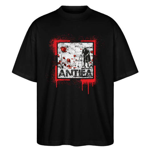 Front view black oversized T‑shirt: Banksy‑inspired red paint‑splatter square framing a grayscale portrait of an elderly person with a walker, scattered red roses and bold ANTHEA wordmark beneath; Stanley/Stella organic unisex.