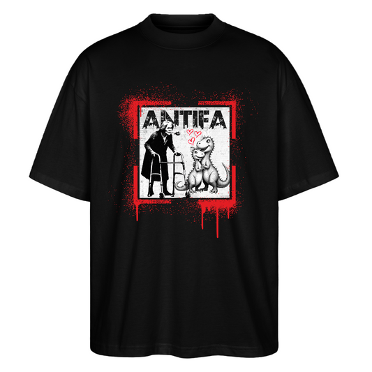 Front view black T‑shirt showing a person using a walker facing a seated dinosaur with pink hearts between them, framed by red paint splatter and distressed white “ANTIFA” print above.